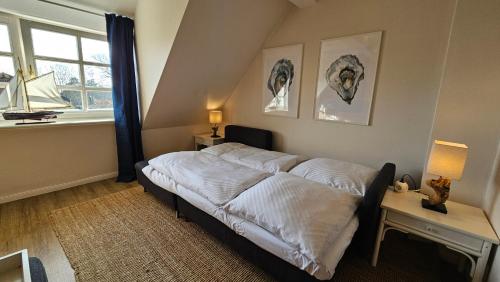 a bedroom with a bed with white sheets and a window at Lazy Osyter Sylt in Braderup