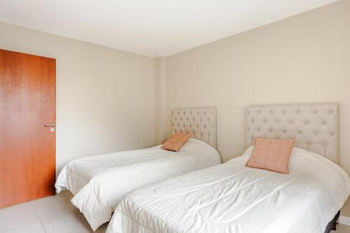 a bedroom with two beds with white sheets and orange pillows at Gray Fox Apartments - San Martin in Ushuaia