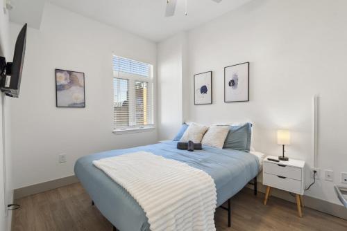 a white bedroom with a blue bed and a window at Cozy City Charm - Spacious, Parking, Balcony, Gym in Charlotte
