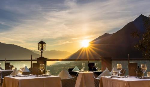 ein Restaurant mit weißen Tischen und Sonne im Hintergrund in der Unterkunft Hotel Panorama in Schenna
