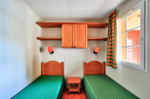 Cette chambre comprend 2 lits verts et une fenêtre. dans l'établissement La résidence du Lac - maeva Home - Appartement 2 pièces 4 personnes - Sélection MAE-4791, à Monflanquin