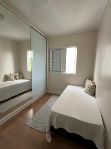 a white bedroom with a bed and a mirror at Apartamento familiar próximo à Universidade in Tubarão