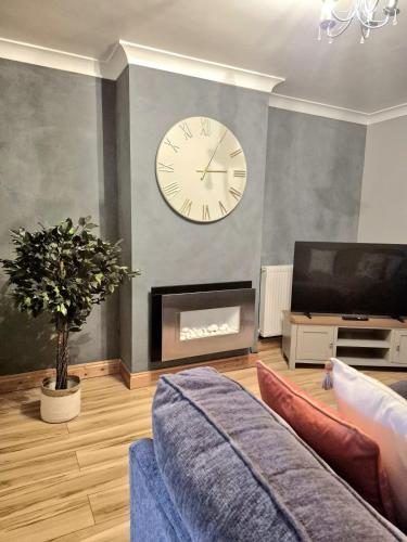 a living room with a clock on the wall and a tv at Large 3-Bed House Near Fosse Park - Free Parking in Leicester