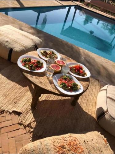 four plates of food on a table next to a pool at L'Hacienda Joud - Privatisation de 5 chambres dans un havre de paix à Marrakech avec piscine & cuisinière privée dans le désert d'Aït Ourir in Aïn er Rmel