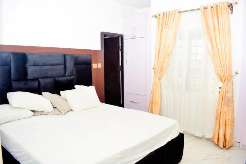 a bedroom with a bed with white sheets and an orange curtain at Ike Service Apartments in Owerri