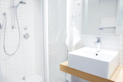 a white bathroom with a sink and a shower at Kleine Brise mit Meerblick und Schwimmbad in Kronsgaard