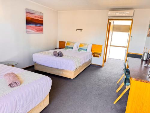 a bedroom with two beds and a door to a balcony at Waikanae Beach Motel in Gisborne