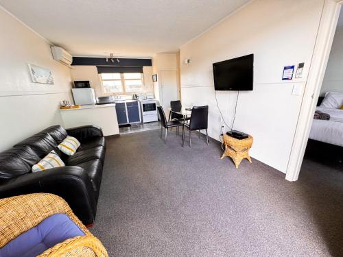 a living room with a black couch and a kitchen at Waikanae Beach Motel in Gisborne