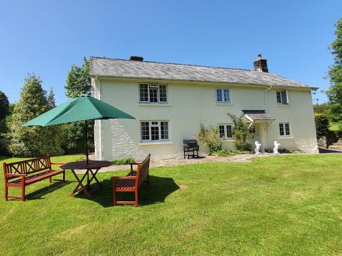 a house with a table and an umbrella in the yard at Wey House Withypool in Withypool