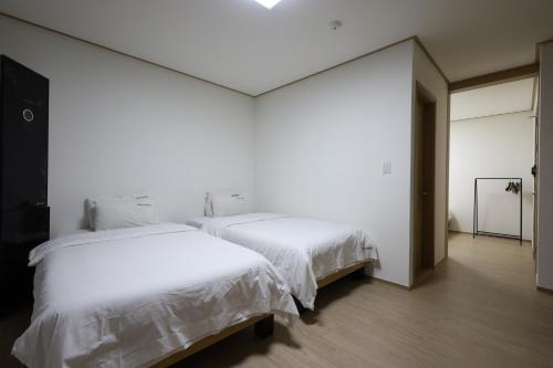 two beds in a room with white walls and wood floors at TRT Hotel in Busan
