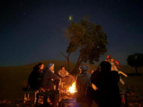 a group of people sitting around a fire at night at Erg Chebbi Star Camp in Merzouga