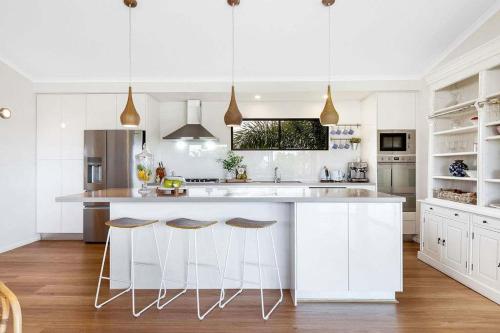 a kitchen with white cabinets and a large island with stools at Luxury 5-Bedroom Canal-Front Retreat in Mooloolaba in Mooloolaba