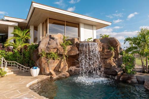 a swimming pool with a waterfall in front of a house at Hale 'O Ka La in Hapuna Beach
