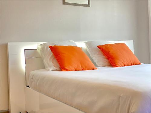 deux oreillers orange posés sur un lit blanc dans l'établissement Joli studio en Résidence boisée Ecully, à Écully