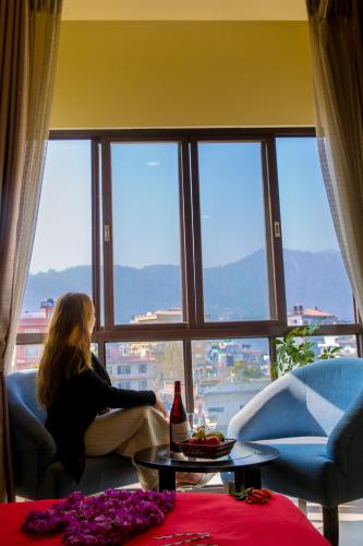 a woman sitting on a couch looking out of a window at Tuki Resort Pokhara in Pokhara