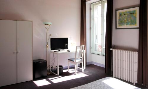 a room with a desk with a television and a chair at Hôtel Adour in Pau