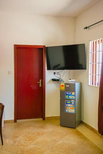 a room with a tv and a refrigerator and a red door at Byblos Hotel-Sky Osu in Accra