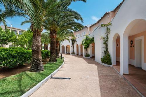 a walkway with palm trees in front of a building at Sol Falco Menorca in Son Xoriguer