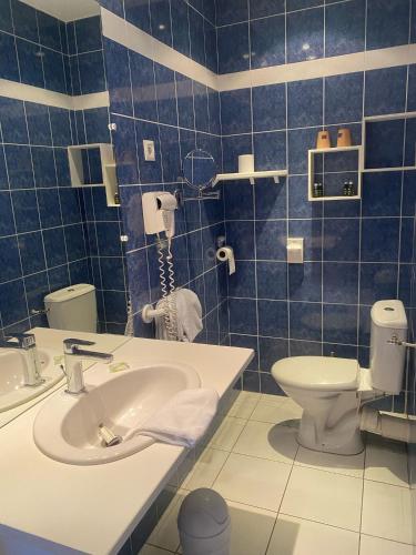 a blue tiled bathroom with a sink and a toilet at Logis Hôtel Restaurant LE MONARQUE in Blois