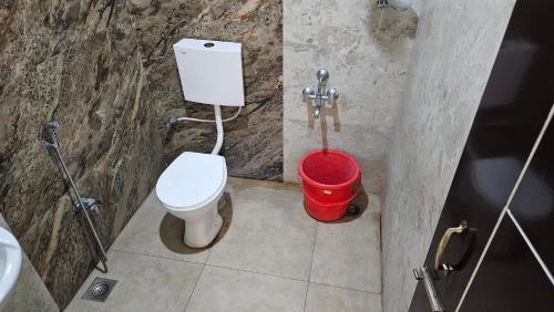 a bathroom with a white toilet and a red bucket at Mookambika Serviced Apartment in Coimbatore