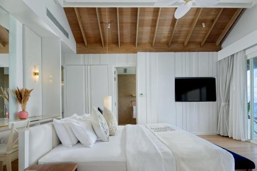 a white bedroom with a white bed and a tv at Bandos Maldives in North Male Atoll
