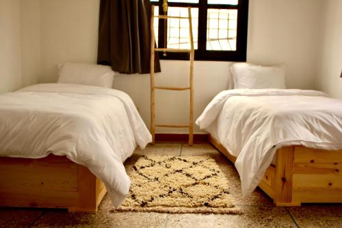 a bedroom with two beds with white sheets and a rug at Azurf - Imsouane Surf House in Imsouane
