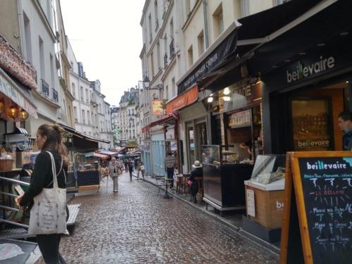 une femme marchant dans une rue de la ville avec des magasins dans l'établissement Belle chambre Rive Gauche, à Paris