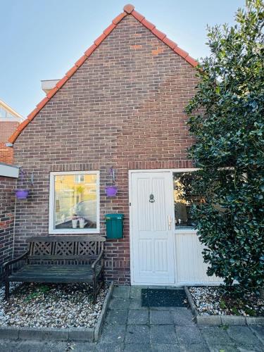 a brick house with a white door and a bench at Strandhuisje Quarles in Noordwijk