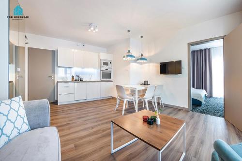 a living room with a couch and a table and a kitchen at Pod Brzozami Apartamenty 5 Mórz in Ustronie Morskie