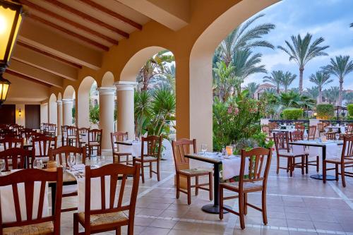 a restaurant with tables and chairs and palm trees at JAZ Almaza Beach Resort, Almaza Bay in Marsa Matruh