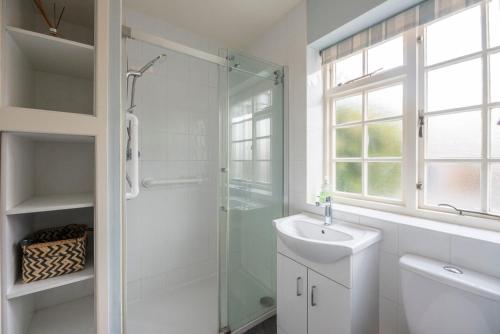 a white bathroom with a shower and a sink at The Little House, Southwold in Southwold