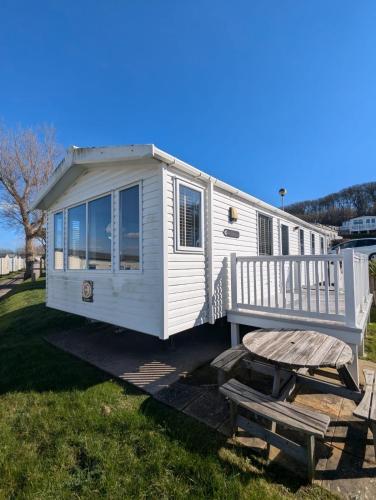 ein weißes winziges Haus mit einer Veranda und einer Schaukel in der Unterkunft BEAUTIFULLY PRESENTED DOG FRIENDLY CARAVAN on VERY POPULAR LITTLESEA HOLIDAY HAVEN PARK WEYMOUTH in Weymouth