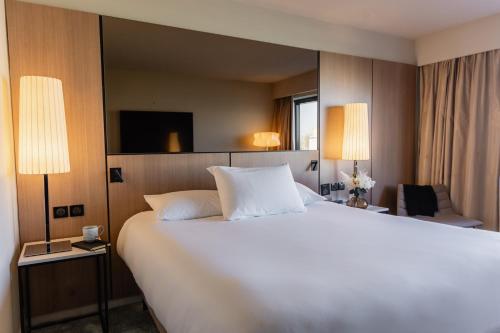 a large white bed in a hotel room with two lamps at Pullman Bordeaux Lac in Bordeaux