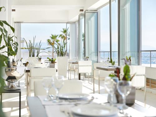 a restaurant with white tables and white chairs and windows at Grecotel LUXME White in Adelianos Kampos