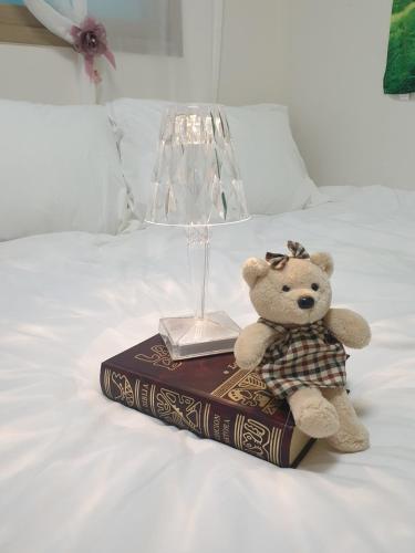a teddy bear sitting on a book next to a lamp at Luna Casa in Daegu