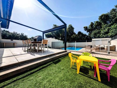 a patio with colorful chairs and a table on the grass at Villa plein Sud, clim et piscine, 6 à 8 personnes in Boisseron