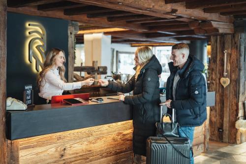 a man and two women shaking hands at a counter at Zermatt Budget Rooms in Zermatt