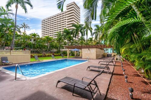 a pool with chairs and palm trees and a building at Honu Hale Penthouse 2 BDR Ocean View Waikiki in Honolulu