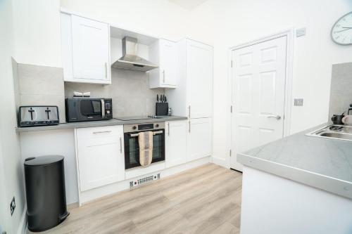 a white kitchen with white cabinets and a sink at The Cheltenham Suites - Elegant 1 Bed Apartment in Cheltenham