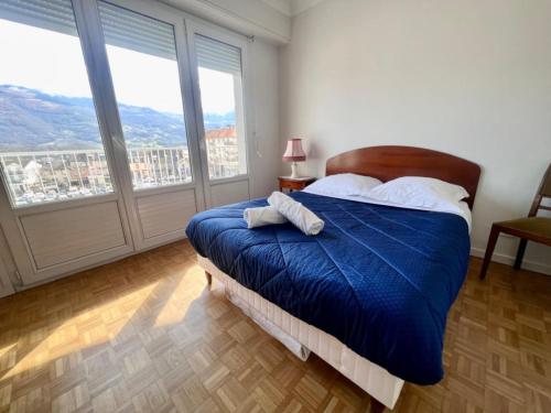 a bedroom with a bed with a blue comforter and large windows at Le balcon du Hautacam in Argelès-Gazost