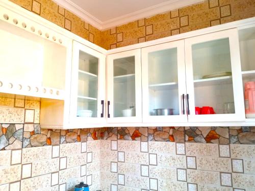 a kitchen with white cabinets on a tiled wall at Bleivory Homes2 in Dar es Salaam