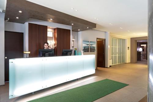 a person sitting at a desk in a lobby at B&B HOTEL Malpensa Lago Maggiore in Vergiate