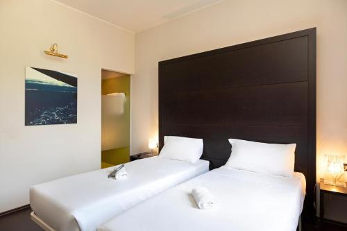 two beds in a hotel room with white sheets at B&B HOTEL Malpensa Lago Maggiore in Vergiate