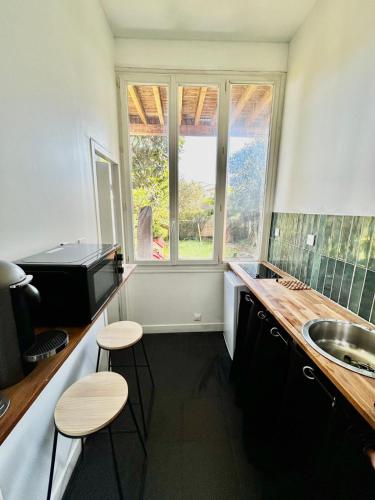 a kitchen with two stools and a sink and two windows at Charmant T2 avec Jardin, Barrière St-Genes in Talence
