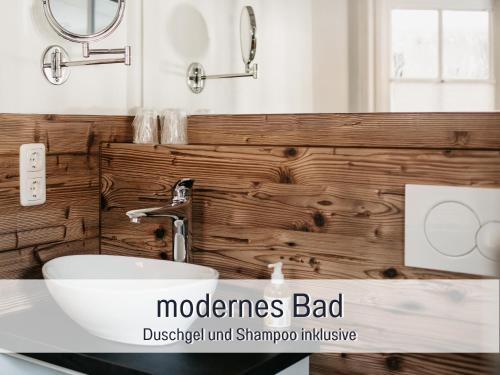 a bathroom with a white sink and a wooden wall at Landhaus Waibelhof in Gunzesried