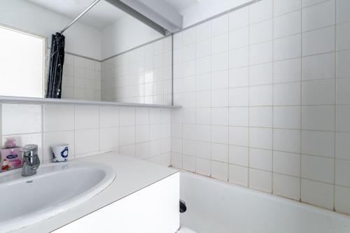 La salle de bains est pourvue de carrelage blanc, d'un lavabo et d'un miroir. dans l'établissement 58 Plein Ouest, Plage Pied, à Pornic