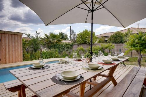 - une table en bois avec un parasol à côté de la piscine dans l'établissement La villa tchanquée du Bassin, à Gujan-Mestras