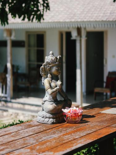 a statue sitting on a wooden table with a bowl of flowers at Villa Olala Penida in Toyapakeh