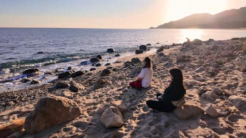 two women sitting on a beach near the water at WakeTheFUP Holistic Meditation Temple in Mas Boquera