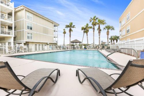 a swimming pool with two chairs and palm trees at Portside 204- Best of Beach & Bay in Orange Beach